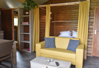 Binnenaanzicht van een houten Cabin met gele zetel en gordijnen op Camping de Koeksebelt in Nederland.