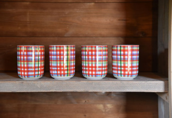 Four colorful plaid cups lined up on a wooden shelf in a cabin at Camping de Koeksebelt in the Netherlands.