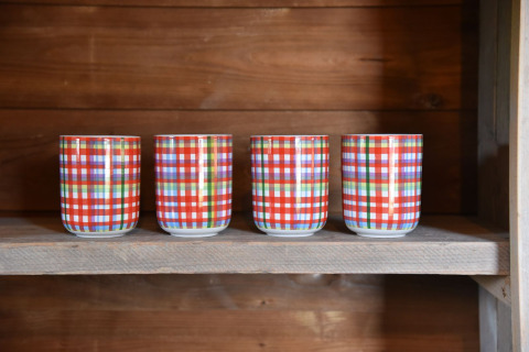 Quatre tasses à carreaux colorées posées sur une étagère en bois dans un chalet au Camping de Koeksebelt, Pays-Bas.