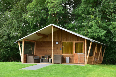 Capanna di legno con veranda coperta e salotto da esterno, tra gli alberi al Camping de Koeksebelt, Paesi Bassi.