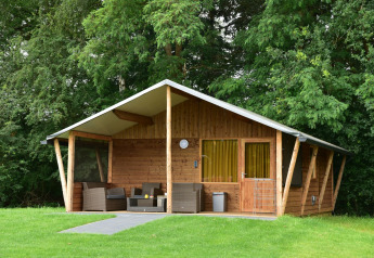 Cabaña de madera con terraza y muebles exteriores rodeada de árboles en Camping de Koeksebelt, Países Bajos.