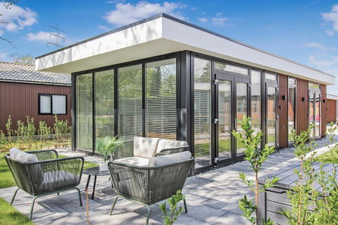 Lodge Forest villa moderna con grandes ventanales, terraza y muebles de jardín bajo un cielo despejado.