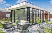 Lodge Forest villa moderna con grandes ventanales, terraza y muebles de jardín bajo un cielo despejado.