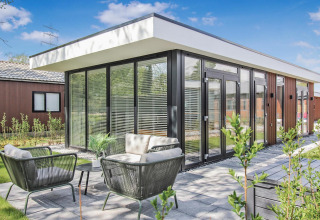 Lodge Forest villa moderna con grandes ventanales, terraza y muebles de jardín bajo un cielo despejado.