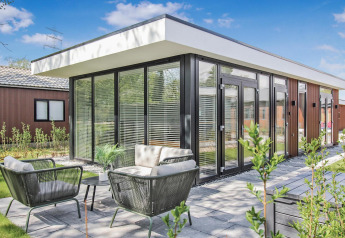 Moderne Forest villa lodge med store glasvinduer, terrasse og udendørs møbler under blå himmel.