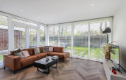 Salón moderno en Forest villa lodge con ventanales, sofá marrón en esquina y vistas al jardín.