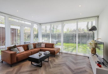 Modern living room at Forest villa lodge with large windows, brown sectional sofa and garden views.