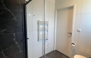 Bagno moderno alla Forest Villa Lodge con box doccia in vetro, piastrelle nere e pareti bianche.