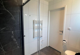 Baño moderno en Forest Villa Lodge con ducha de vidrio, azulejos negros y paredes blancas.