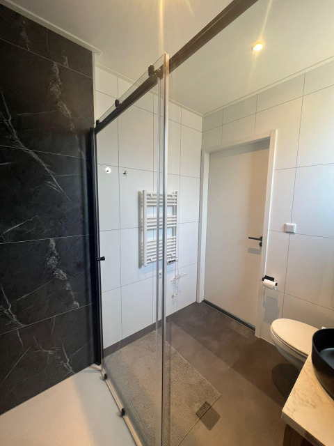 Moderne badeværelse i Forest Villa Lodge med glasbruser, sort vægflise og hvidt vægpanel.