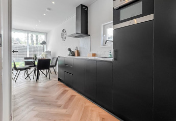 Cocina moderna en el lodge Forest villa con armarios negros, suelo de madera y comedor junto a la ventana.