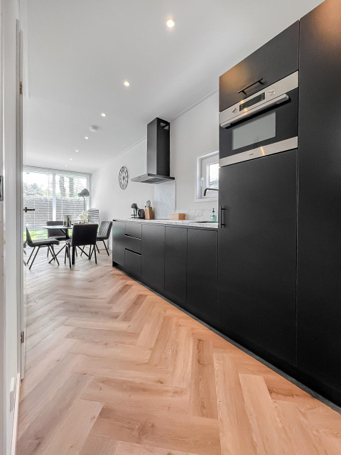 Cocina moderna en el lodge Forest villa con armarios negros, suelo de madera y comedor junto a la ventana.
