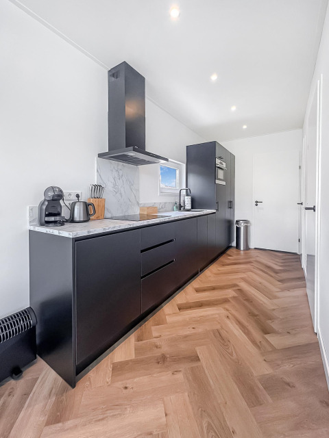 Cocina moderna en Forest villa lodge con gabinetes negros, encimera de mármol y suelo de madera.