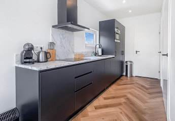 Modern kitchen interior at Forest villa lodge featuring black cabinets, marble countertop, and wood floor.