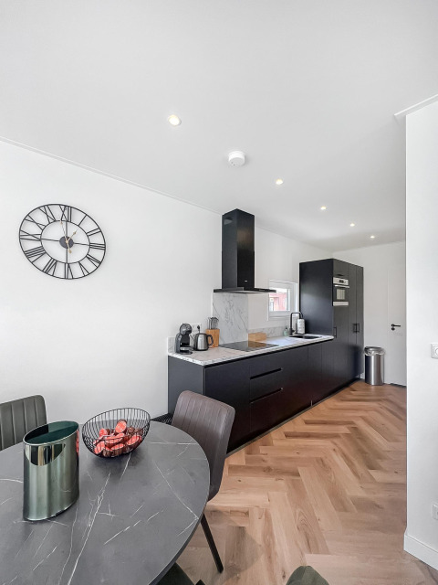 Cocina moderna y comedor en Forest villa lodge con armarios negros, mesa de mármol y reloj en la pared.