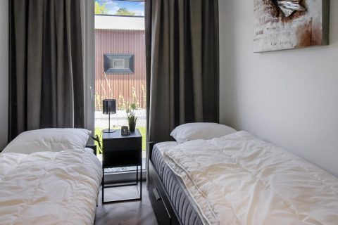 Moderne dobbeltværelse på Forest villa-lodge med to enkeltsenge, natbord og stort vindue.