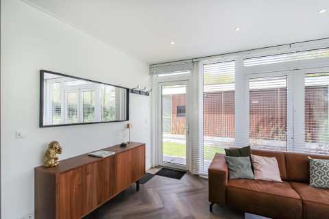 Moderne zithoek in Forest villa lodge met houten kast, bruine zetel en grote ramen met tuinzicht.