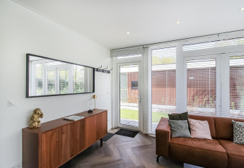 Modern living area in Forest villa lodge with wood cabinet, brown sofa, large windows, and garden view.