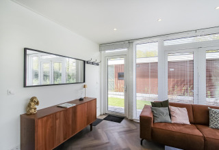 Moderne stue i Forest villa-lodge med træskænk, spejl, sofa og store vinduer med udsigt til haven.