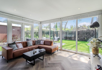 Heldere woonkamer in Forest villa lodge met bruine bank, grote ramen en uitzicht op de tuin.