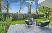 Moderne terrasse ved Forest villa med havemøbler, smuk græsplæne og frodig, grøn indhegning.
