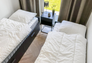 Two single beds in a small, bright room with large windows at the Forest Villa lodge, modern decor.