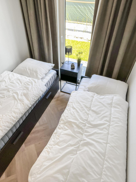 To enkeltsenge i et lille, lyst værelse med store vinduer og et natbord, set på Forest villa lodge.