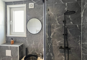 Baño moderno en Forest Villa con lavabo negro, ducha y paredes grises de imitación mármol.