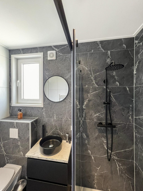 Baño moderno en Forest Villa con lavabo negro, ducha y paredes grises de imitación mármol.