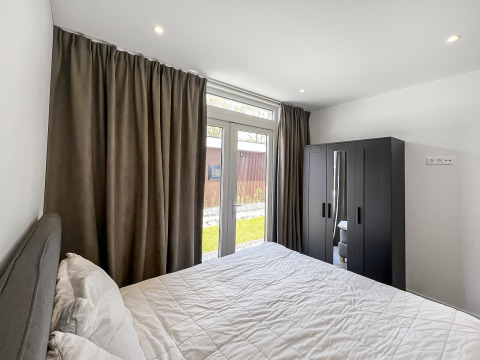 Soveværelse på Forest villa med dobbeltseng, mørke gardiner, klædeskab og udsigt til haven.