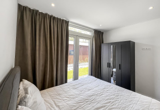 Dormitorio en Forest villa con cama doble, cortinas oscuras, armario y vistas al jardín exterior.