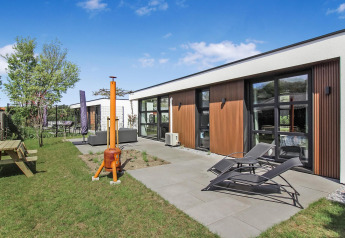 Moderne Forest villa ved Uniq Leisure, Holland, med loungeområde, liggestole og grøn have under blå himmel.