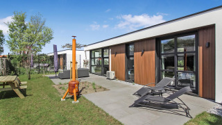 Villa Forest moderne à Uniq Leisure, Pays-Bas, avec chaises longues, terrasse et pelouse verdoyante.