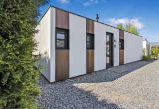 Moderne lodge ved Forest villa på Uniq Leisure i Holland, med hvid facade og træpaneler, solrig dag.