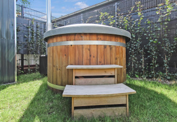 Wooden hot tub with metal bands and steps on grass at the Forest villa at Uniq Leisure, Netherlands.
