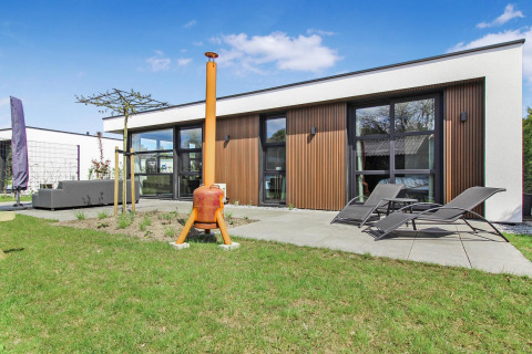 Lodge moderno en Forest villa Uniq Leisure en los Países Bajos con terraza, tumbonas y césped verde afuera.