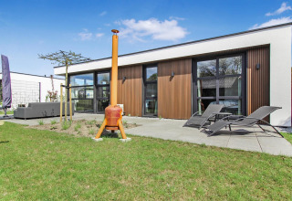 Lodge moderno en Forest villa Uniq Leisure en los Países Bajos con terraza, tumbonas y césped verde afuera.