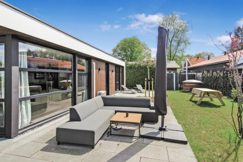 Zona de estar exterior en Eco Lodge de Uniq Leisure en Países Bajos con sofá, sombrilla y jardín verde.