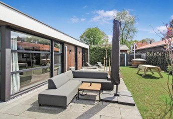 Zona de estar exterior en Eco Lodge de Uniq Leisure en Países Bajos con sofá, sombrilla y jardín verde.