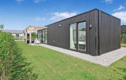 Eco Lodge moderna en Uniq Leisure, Países Bajos, con fachada de madera oscura y gran jardín verde.