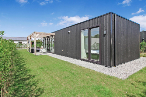 Eco Lodge moderna en Uniq Leisure, Países Bajos, con fachada de madera oscura y gran jardín verde.