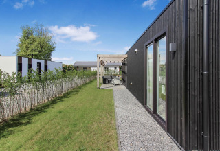 Moderne hytte ved Eco Lodge på Uniq Leisure i Holland med sort facade, have og terrasse under klar himmel.