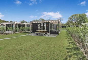 Eco Lodge en Uniq Leisure, Países Bajos, con una moderna cabaña, césped verde y área de terraza cubierta.