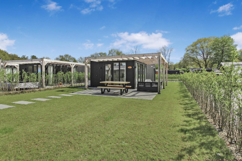Eco Lodge en Uniq Leisure, Países Bajos, con una moderna cabaña, césped verde y área de terraza cubierta.