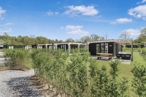 Eco Lodge ved Uniq Leisure i Holland, sorte træhytter med store vinduer, terrasse og have under blå himmel.