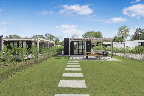 Eco Lodge moderna en Uniq Leisure, Países Bajos, con jardín, sendero y terraza exterior con bancos.