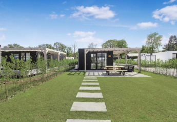 Eco Lodge moderna en Uniq Leisure, Países Bajos, con jardín, sendero y terraza exterior con bancos.