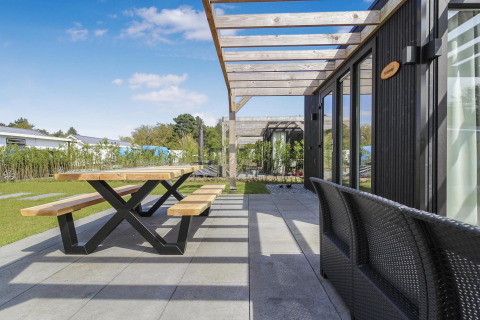 Terraza exterior en Eco Lodge, Uniq Leisure, Países Bajos, con mesa y bancos de madera bajo pérgola moderna.