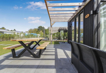 Terraza exterior en Eco Lodge, Uniq Leisure, Países Bajos, con mesa y bancos de madera bajo pérgola moderna.