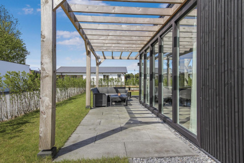 Terraza moderna con paredes de cristal y pérgola de madera en Eco Lodge de Uniq Leisure, Países Bajos.